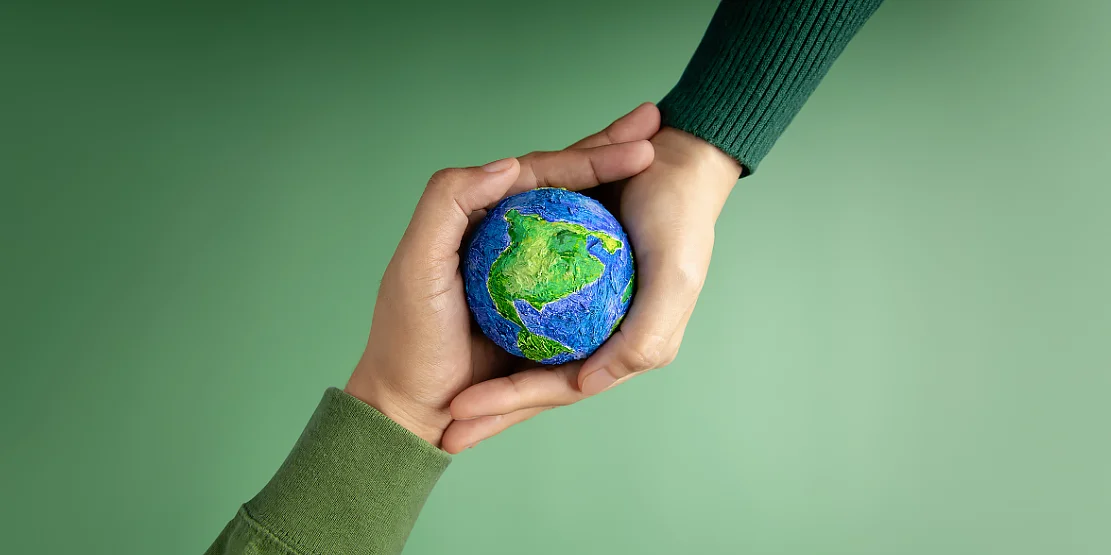 Benefícios para o Meio Ambiente, representado por um mini-planeta Terra e duas mãos que o seguram, em um fundo verde.